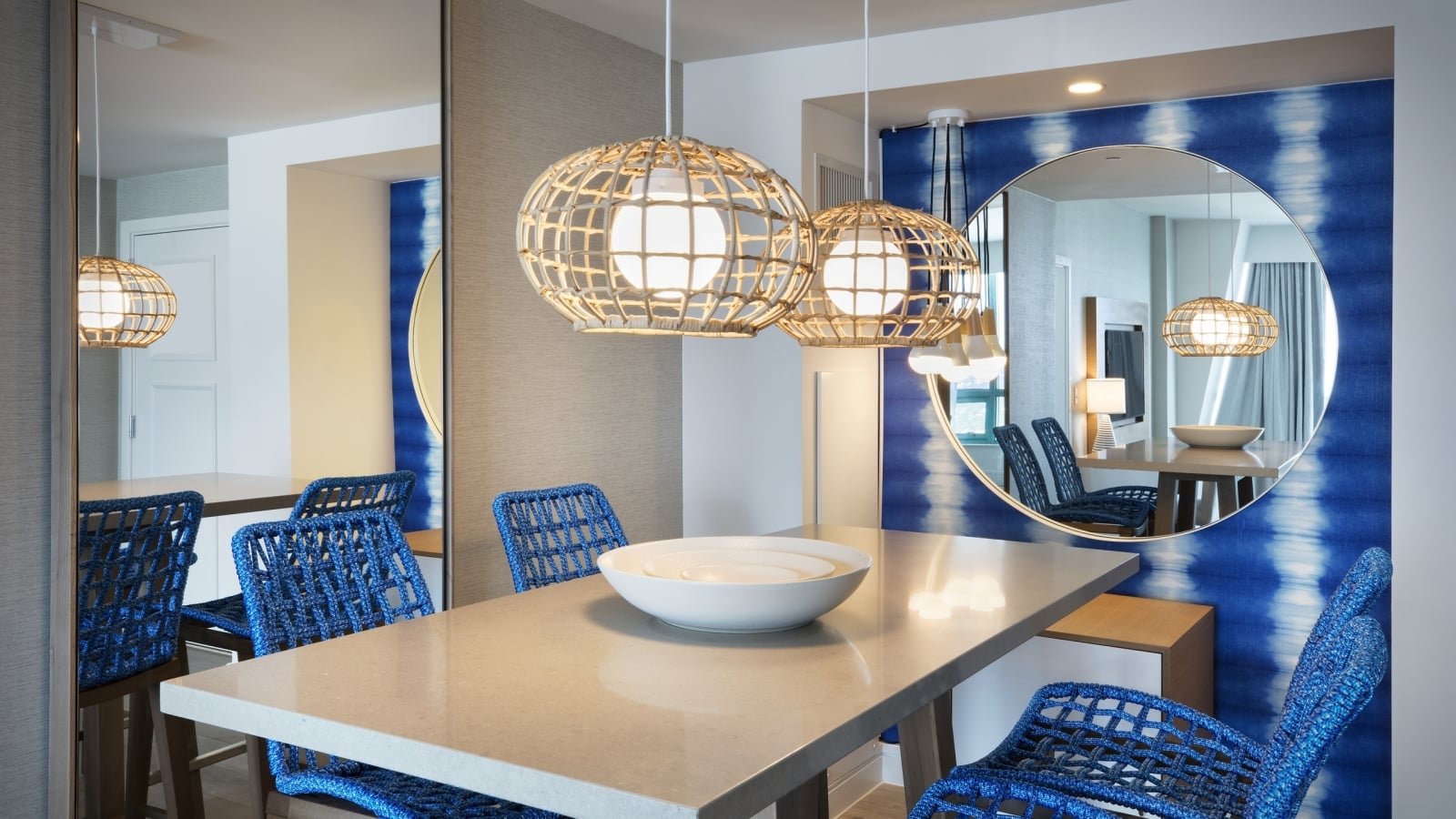 Dining table in the Diplomat Suite with hanging lights, blue chairs and a round circular mirror hung on the wall