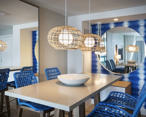 Dining table in the Diplomat Suite with hanging lights, blue chairs and a round circular mirror hung on the wall