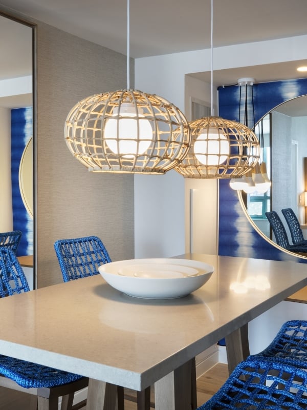Dining table in the Diplomat Suite with hanging lights, blue chairs and a round circular mirror hung on the wall
