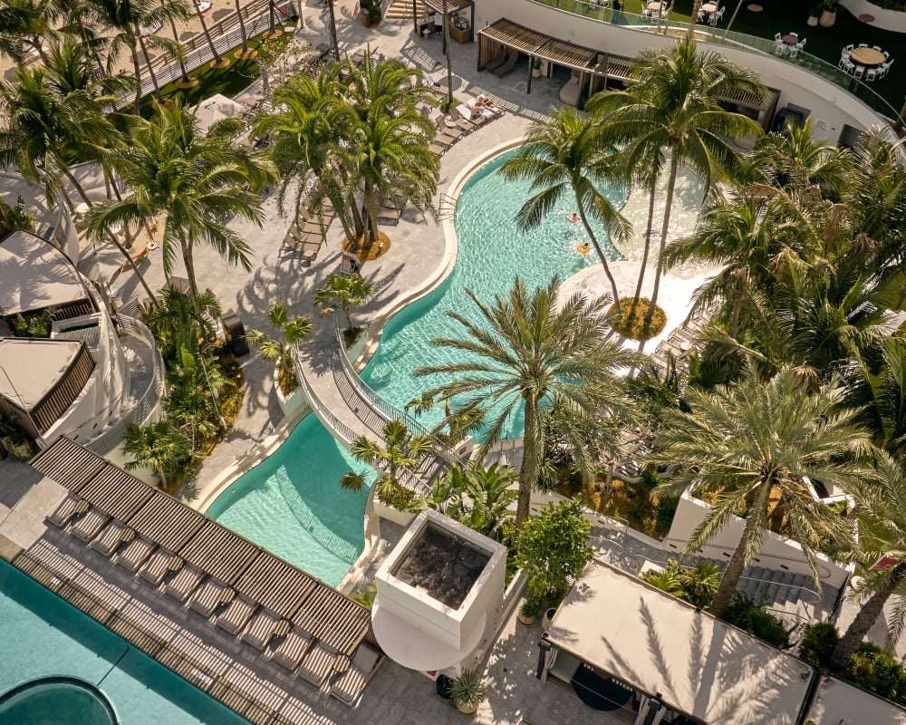 Aerial view of The Diplomat outdoor pools surrounded by palm trees, cabanas, and lounge chairs
