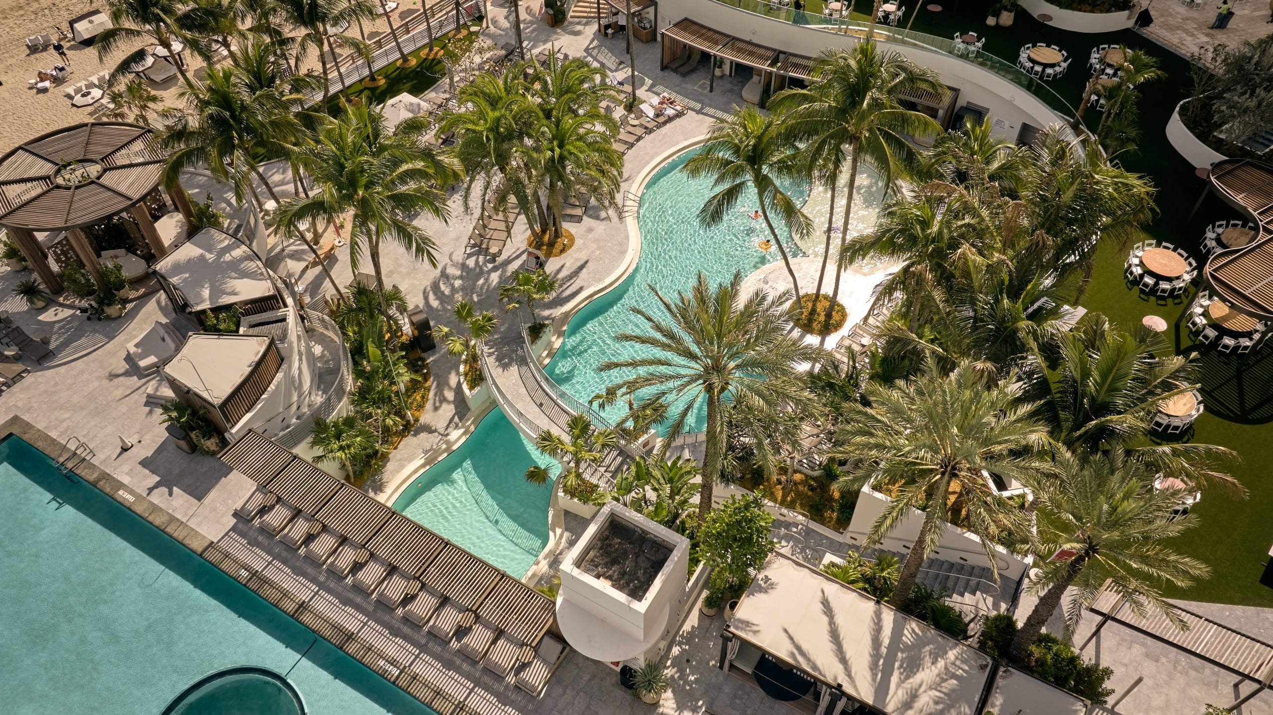 Aerial view of The Diplomat outdoor pools surrounded by palm trees, cabanas, and lounge chairs