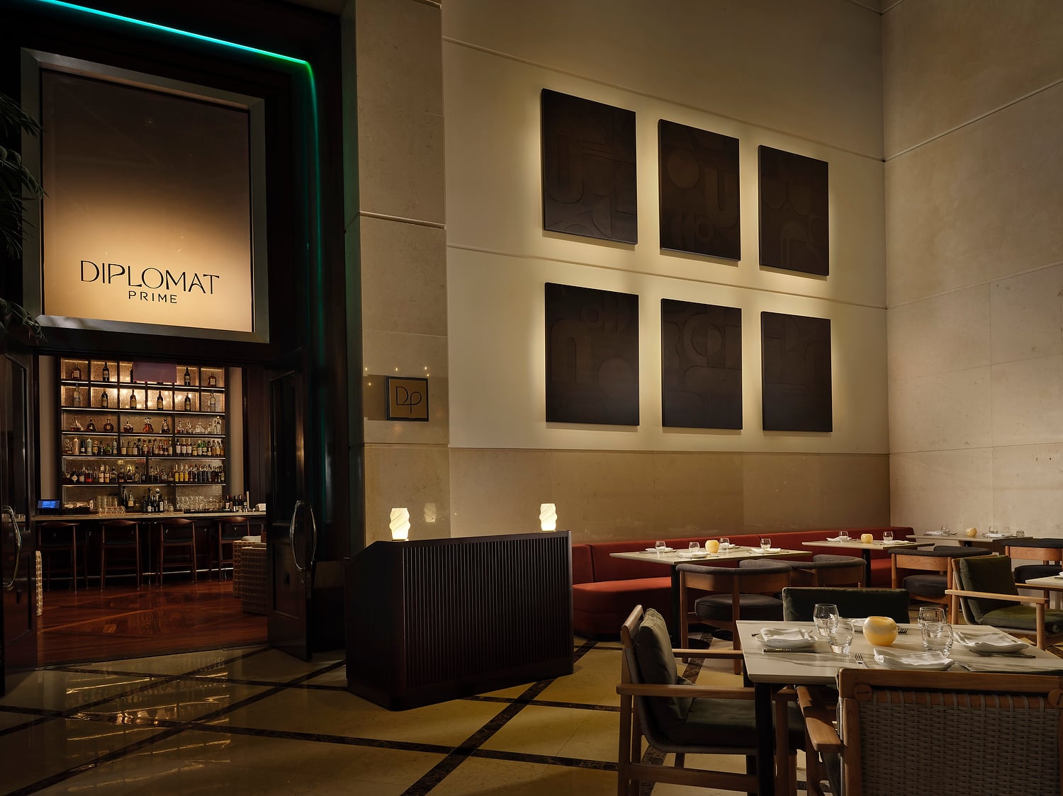 A warmly lit restaurant entrance with a backlit sign reading "DIPLOMAT PRIME" and a "DP" plaque, opens to a full bar and a dining room with set tables and six dark abstract artworks.