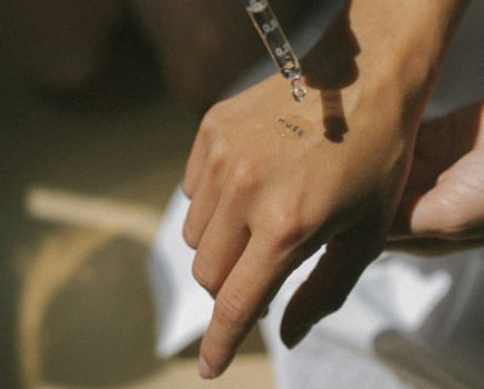 A hand receives a liquid drop from a glass dropper. "MUSE" is written on the hand, illuminated by warm natural light.