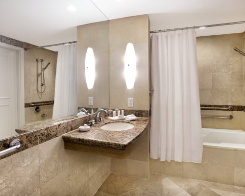 Guestroom bathroom with accessible tub with hand rails at various heights, and a floating vanity sink