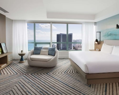 Presidential Suite bedroom featuring a king bed, large oval lounge chair, mounted TV, and modern decor