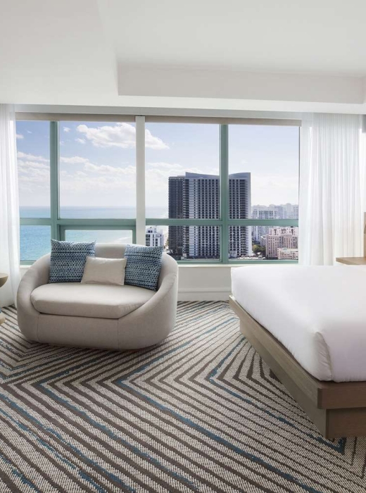 Presidential Suite bedroom featuring a king bed, large oval lounge chair, mounted TV, and modern decor
