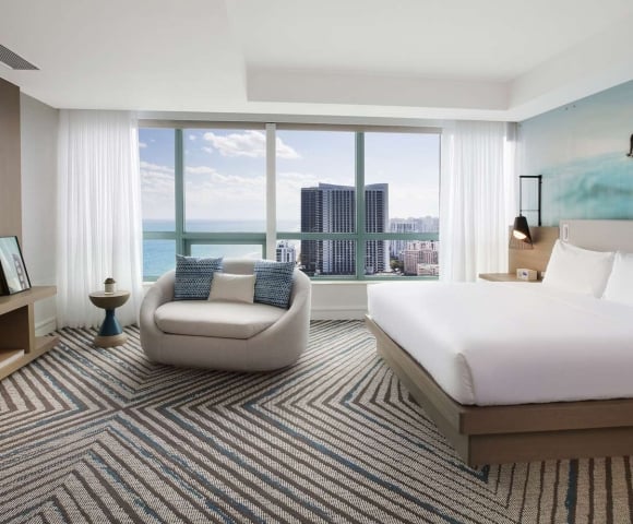 Presidential Suite bedroom featuring a king bed, large oval lounge chair, mounted TV, and modern decor