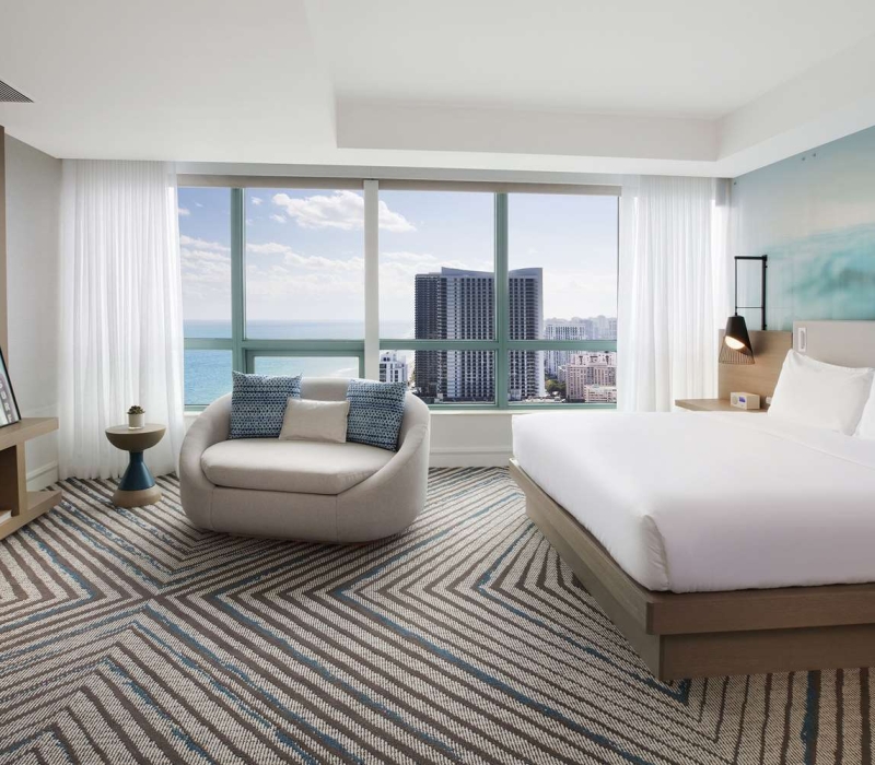 Presidential Suite bedroom featuring a king bed, large oval lounge chair, mounted TV, and modern decor