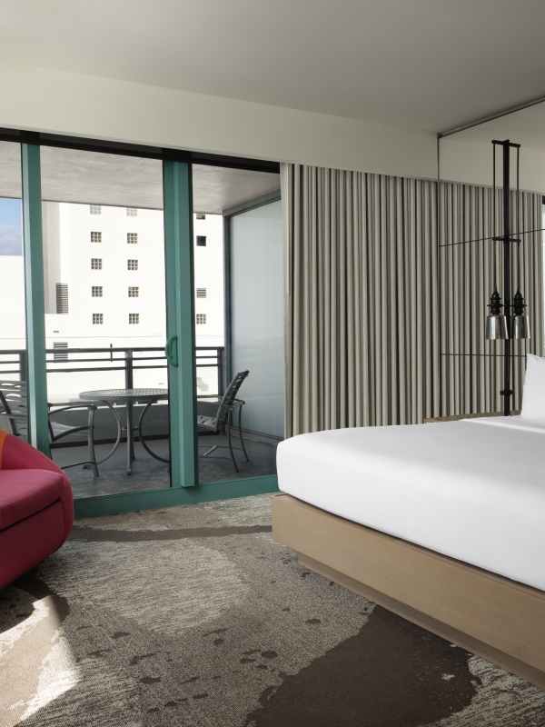 Corner king accommodation featuring white linens, a large red lounge chair, and floor to ceiling windows that look onto the patio and surrounding area.