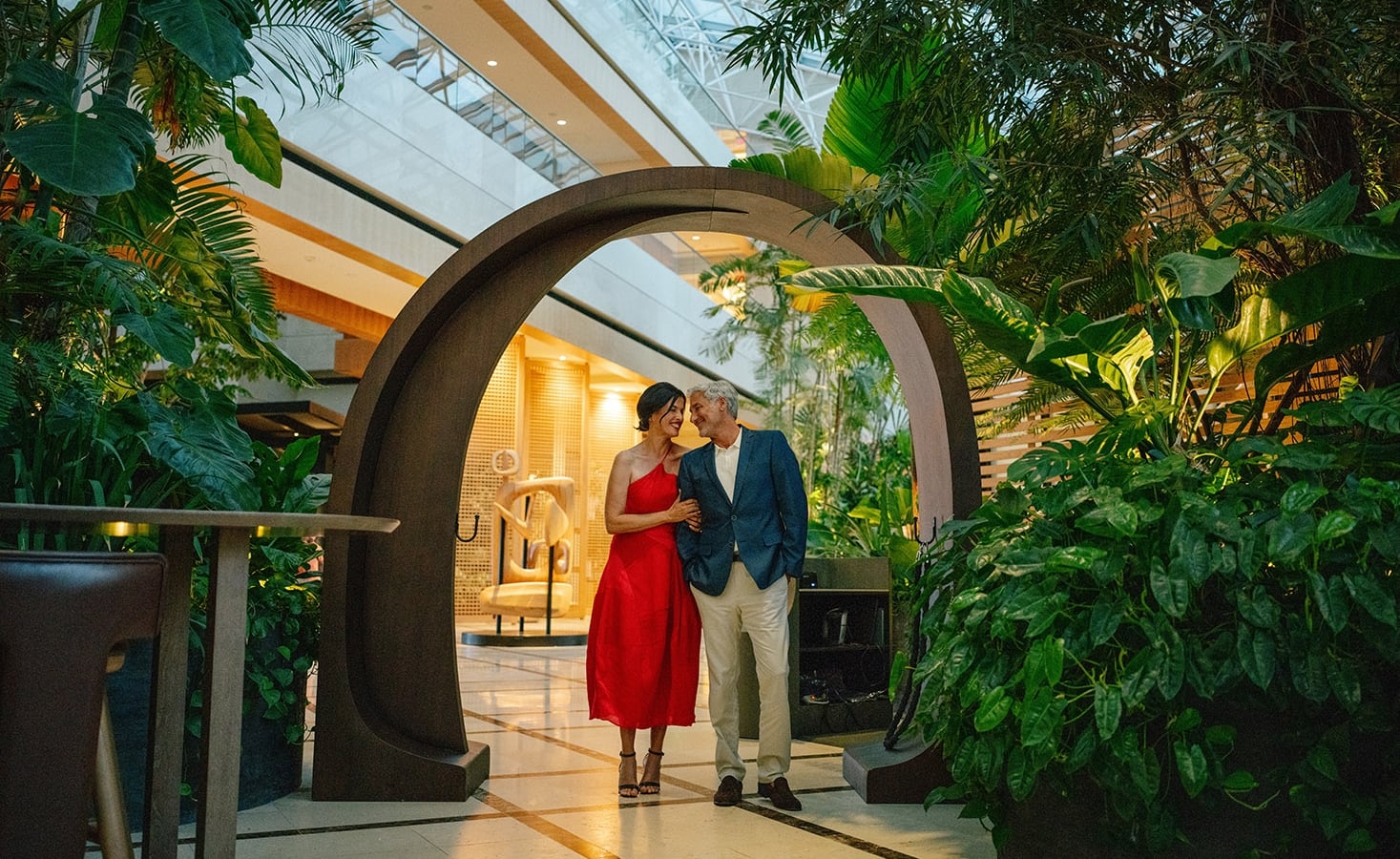 A well dressed couple smile at each other under a round decorative archway