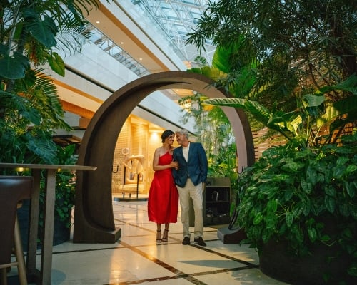 A well dressed couple smile at each other under a round decorative archway