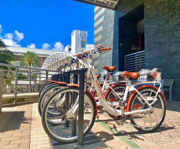 A row of white and orange "The DIPLOMAT BEACH RESORT" bicycles are parked on a paved plaza next to a dark building. Text: 3555 SOUTH OCEAN DRIVE, CAUTION SLIPPERY FLOOR.