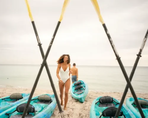 A couple preparing to kayak on the ocean. The man heads towards the ocean, kayak in tow, while the woman heads back to grab her kayak.