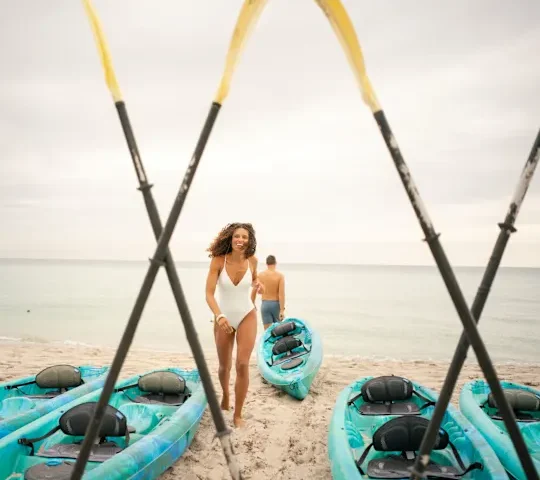 A couple preparing to kayak on the ocean. The man heads towards the ocean, kayak in tow, while the woman heads back to grab her kayak.