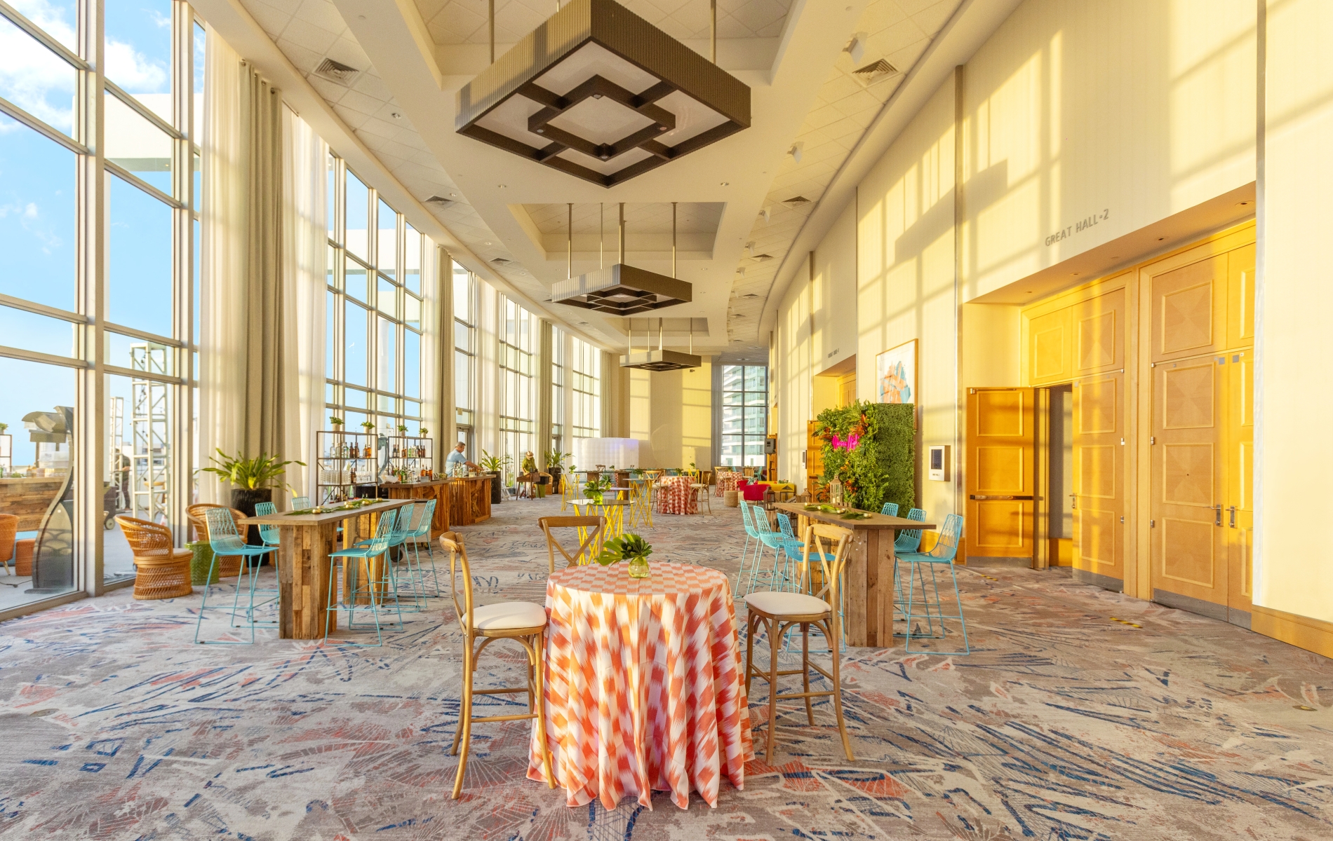 Great Hall Preassembly event space with floor-to-ceiling windows, patterned carpet, cocktail tables and teal bistro chairs.