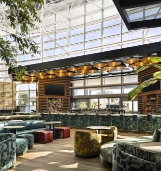 Solara bar with a glass atrium ceiling, lush greenery, patterned seating, and a green-tiled bar with gold pendant lights.