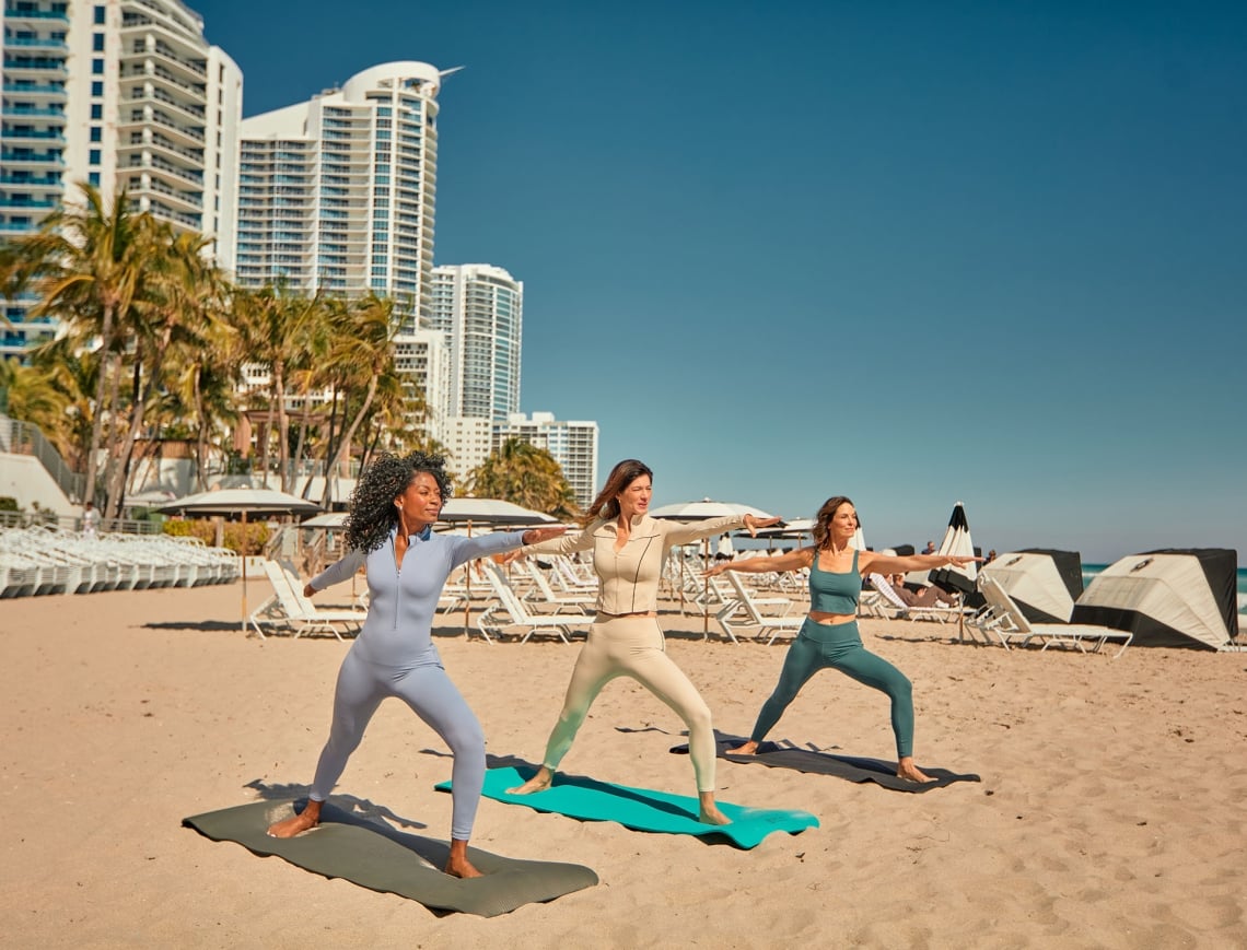 Three woman in athletic wear performing yoga on the beach