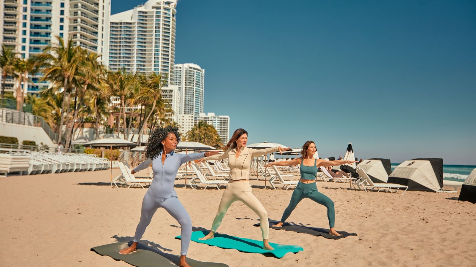 Three woman in athletic wear performing yoga on the beach
