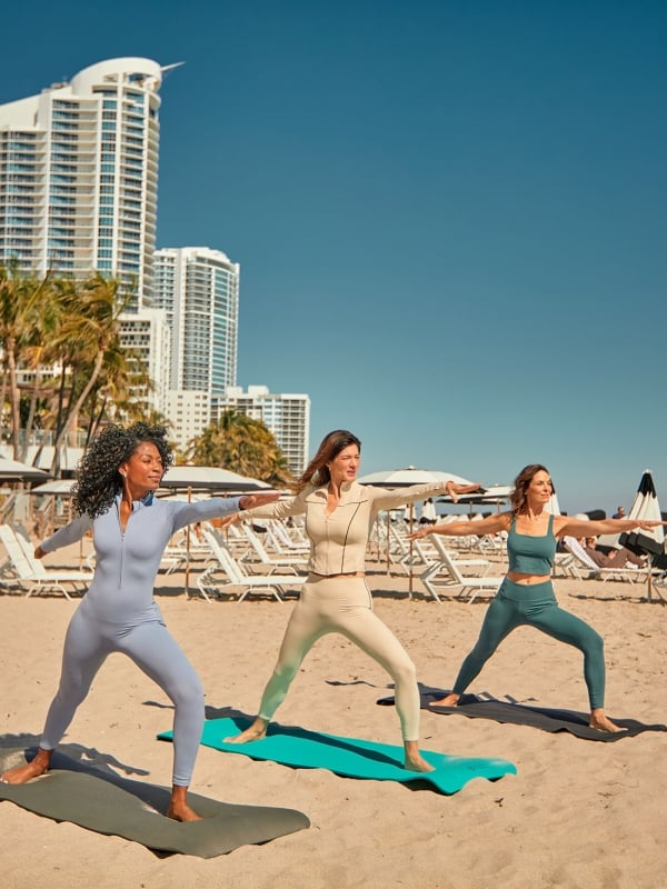 Three woman in athletic wear performing yoga on the beach